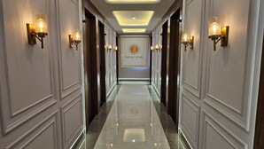 A hotel hallway with a polished marble floor, wall-mounted sconces, and a central emblem. - The Blu Pearl (Gwalior)
