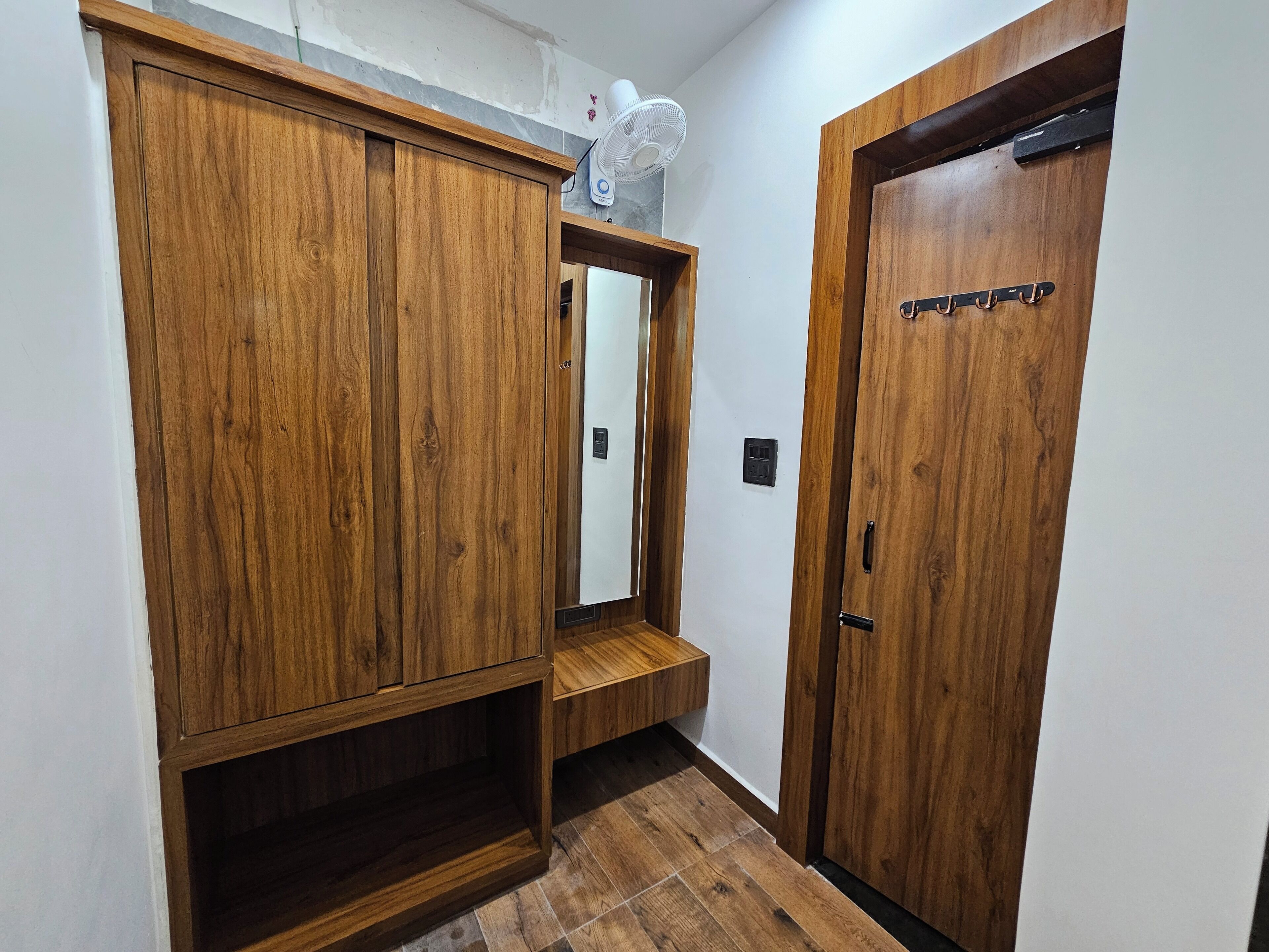 Um corredor com armários de madeira, um espelho e uma porta com ganchos.