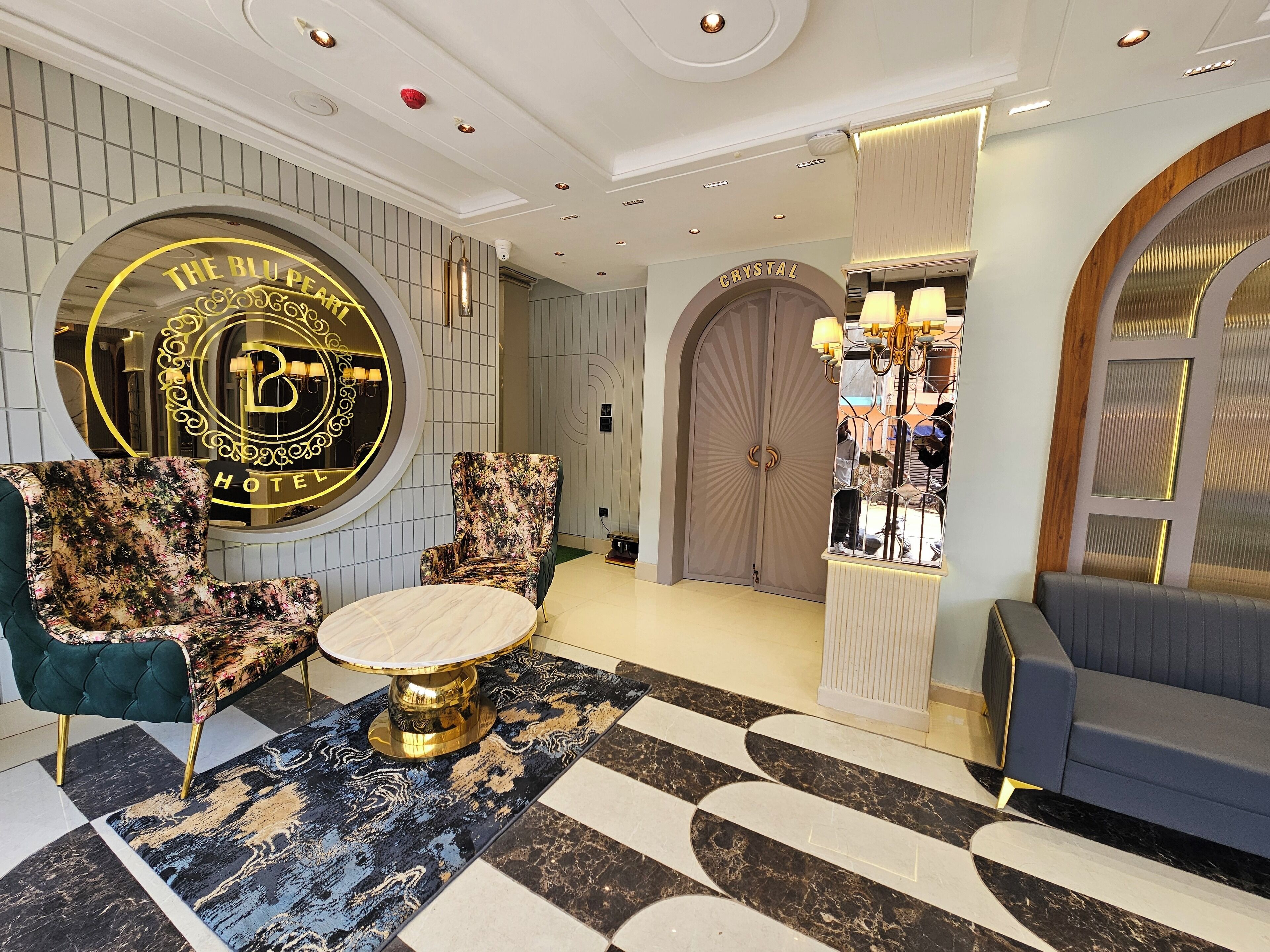 A hotel lobby with a round table, two armchairs, a sofa, and a large mirror.