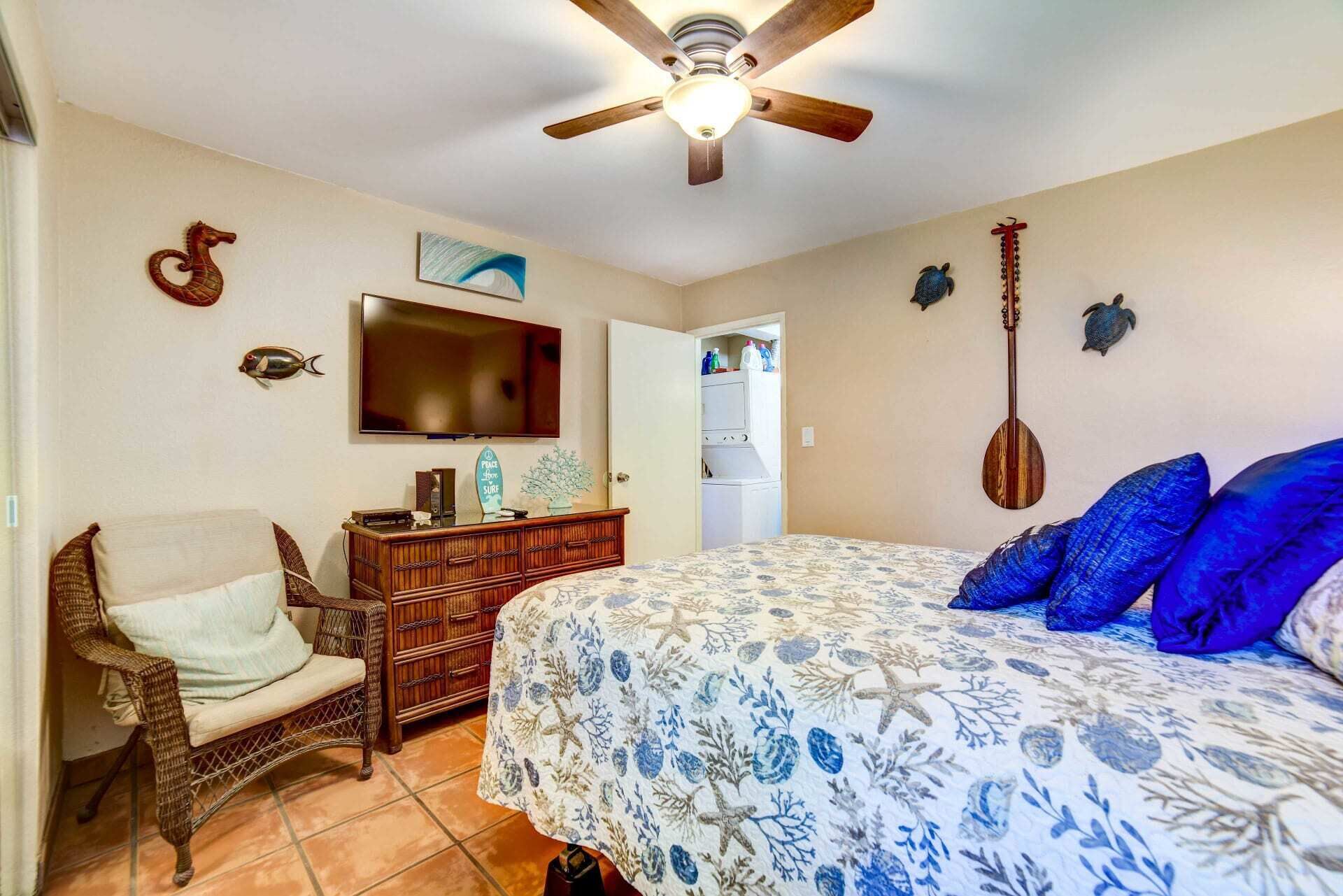 Une chambre à coucher comprenant un lit, une chaise, une commode, un téléviseur et un ventilateur de plafond.