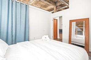 A bedroom with a large bed, a wooden ceiling, a blue curtain, and a mirror reflecting a window. - Pet Friendly | King Bed | Beltline Access (Atlanta)