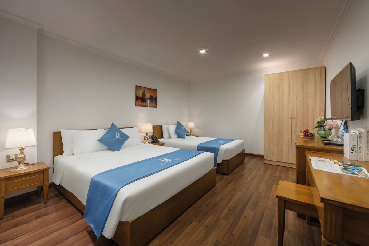 Una habitación de hotel con dos camas, un escritorio, un televisor y un cuadro en la pared.