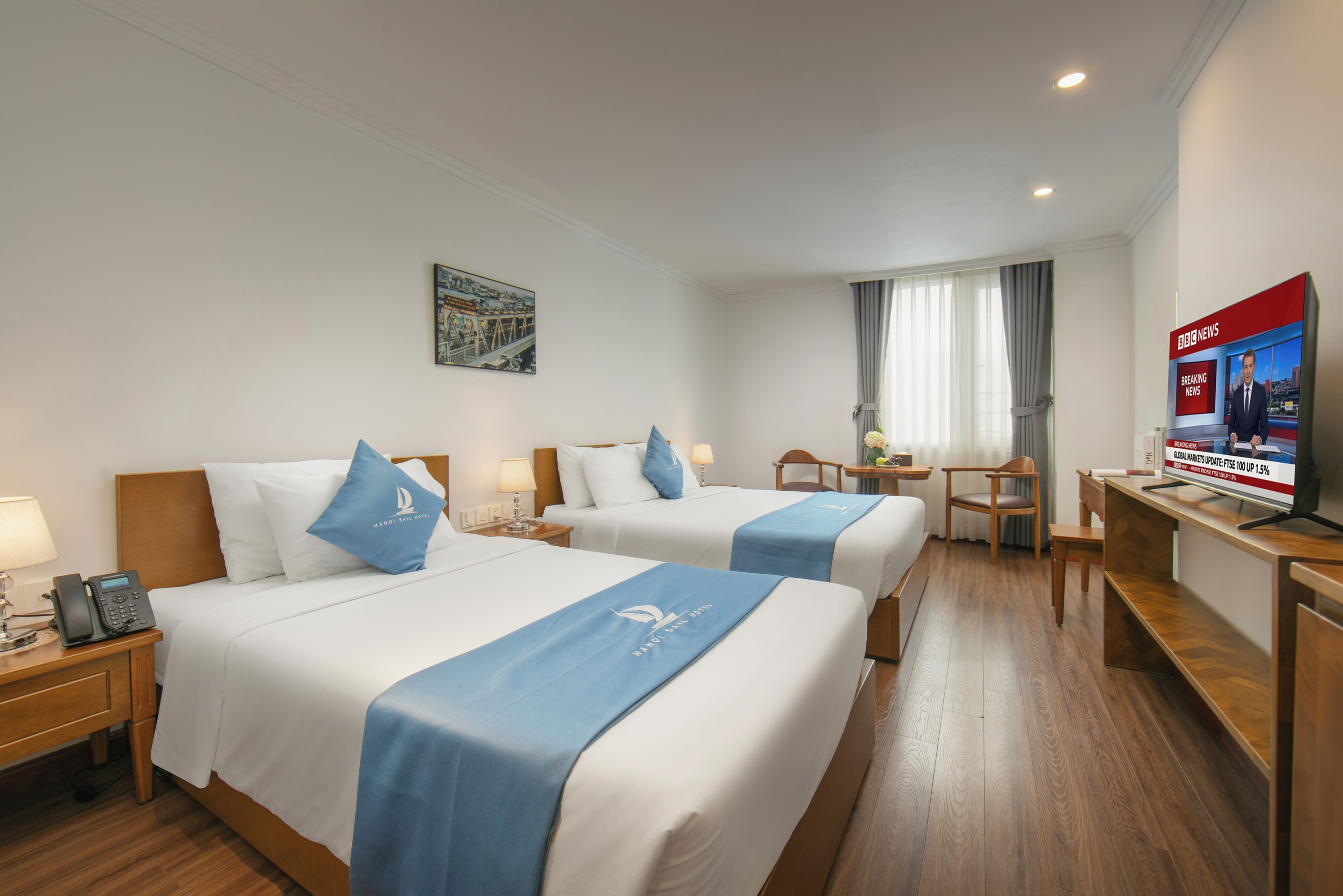 Habitación de hotel con dos camas, un escritorio, una silla, un televisor y una ventana con cortinas.