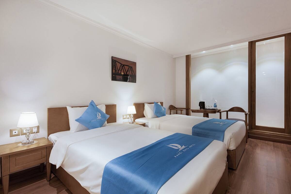 Habitación de hotel con dos camas, una mesita de noche, un escritorio y un ventanal grande.