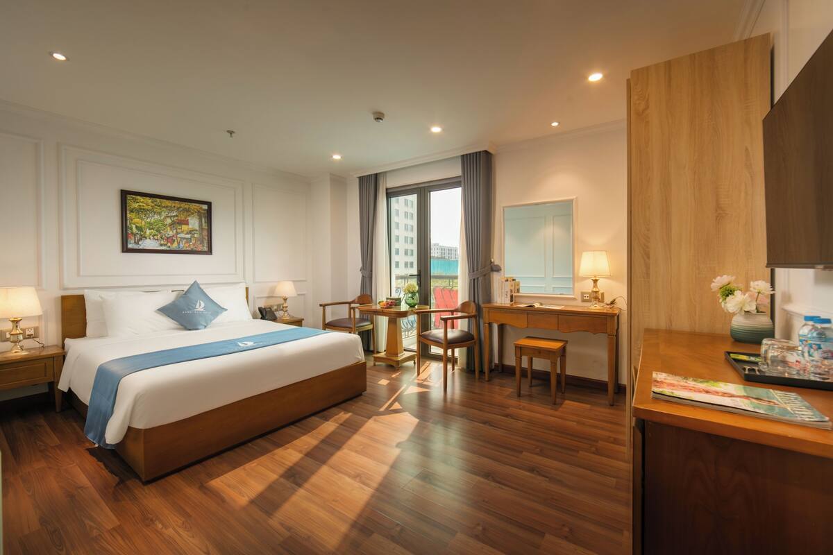 Habitación de hotel con una cama grande, un escritorio, una silla, una mesita y una ventana con cortinas.