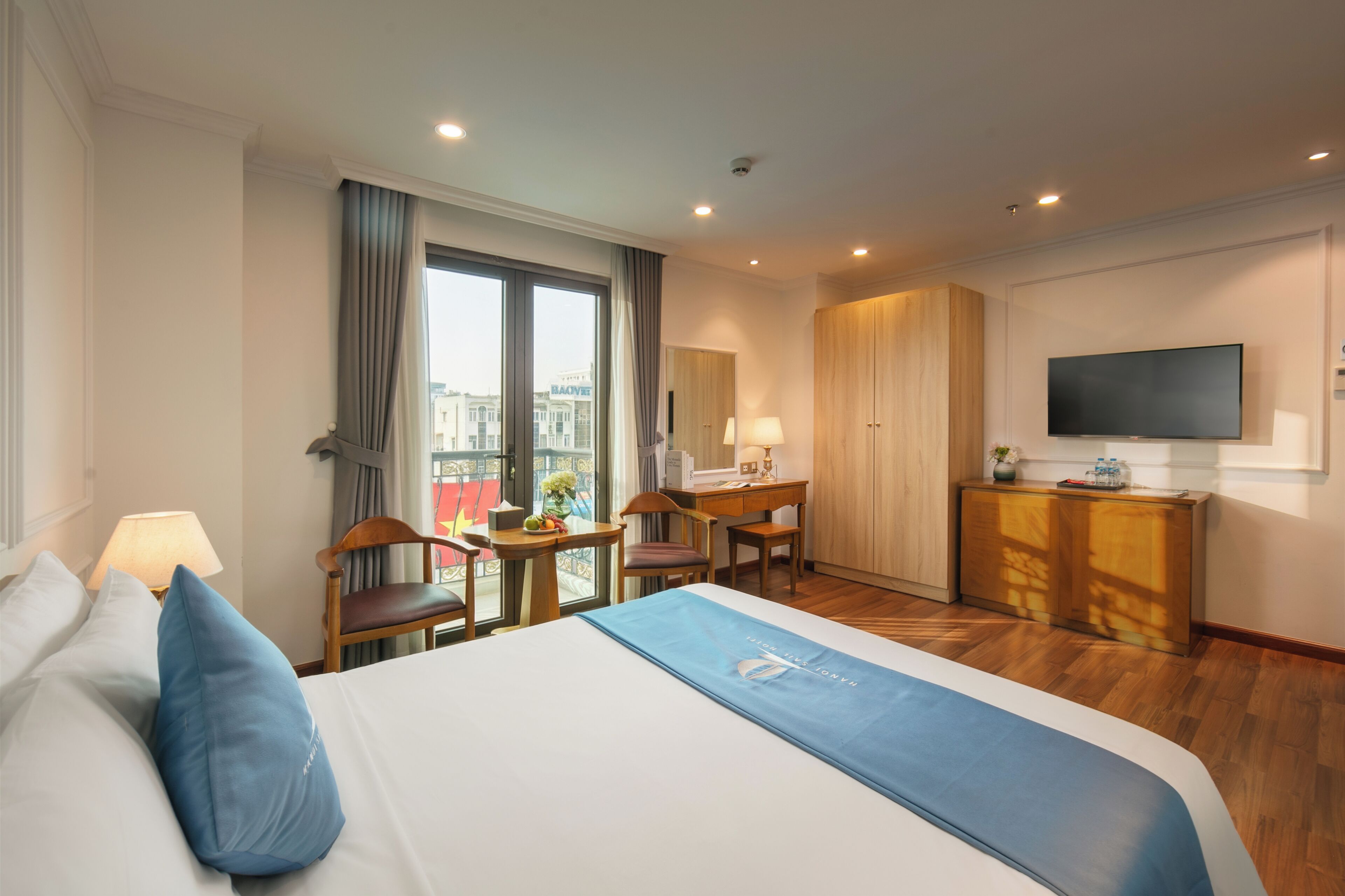 Een hotelkamer met een bed, bureau, stoel, televisie, kledingkast en uitzicht op de stad.