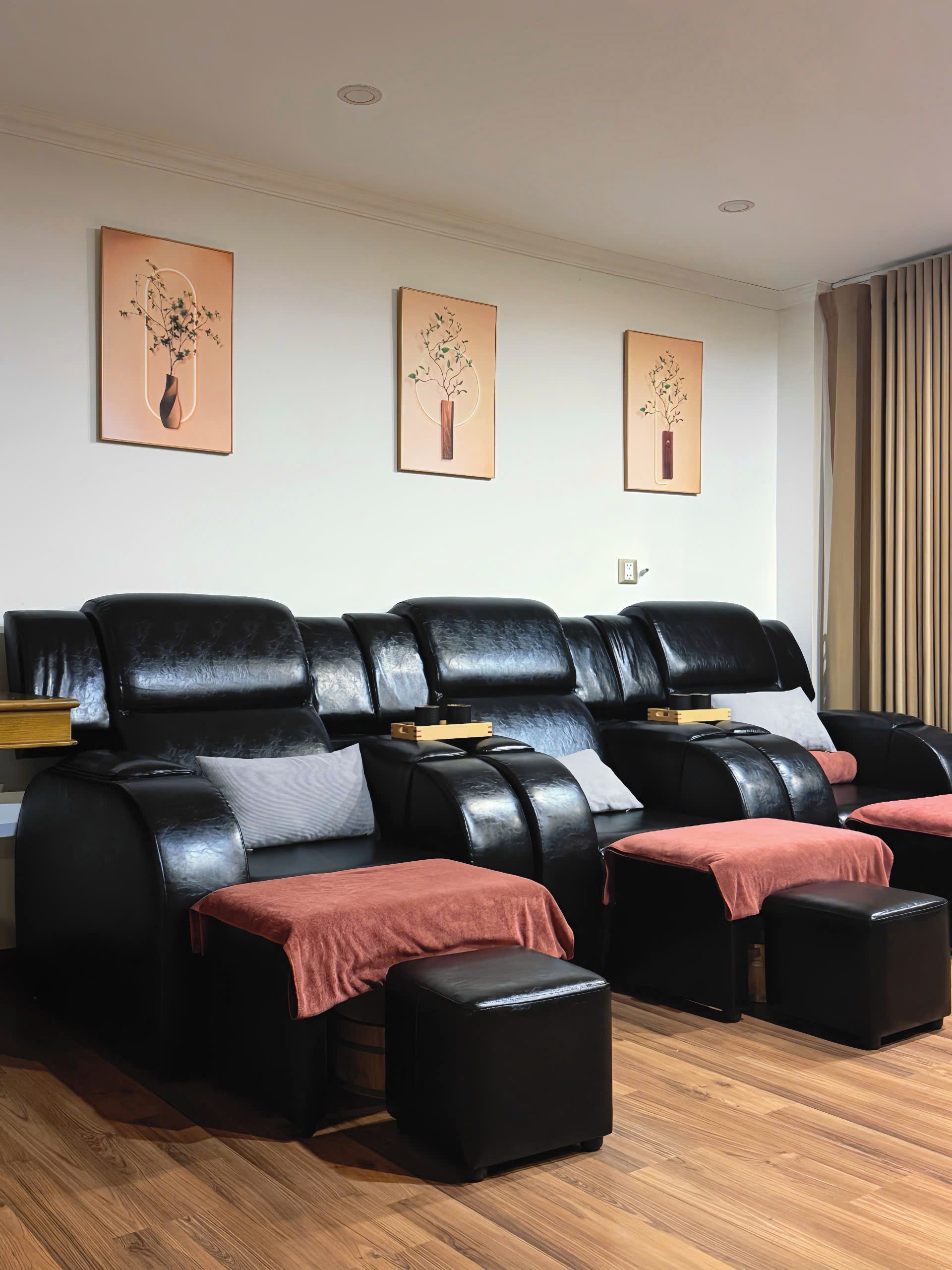 A massage room with black leather massage chairs, a wooden floor, and three wall-mounted artwork.