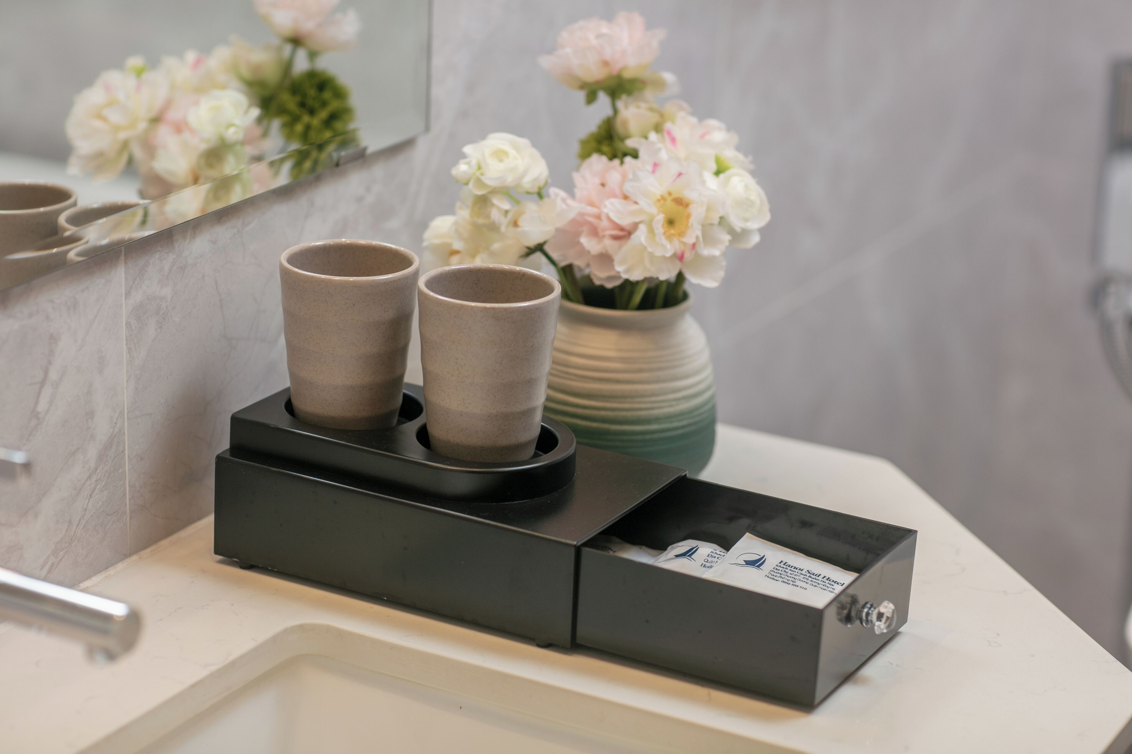 A bathroom with a mirror, a vase of flowers, and a soap dispenser.