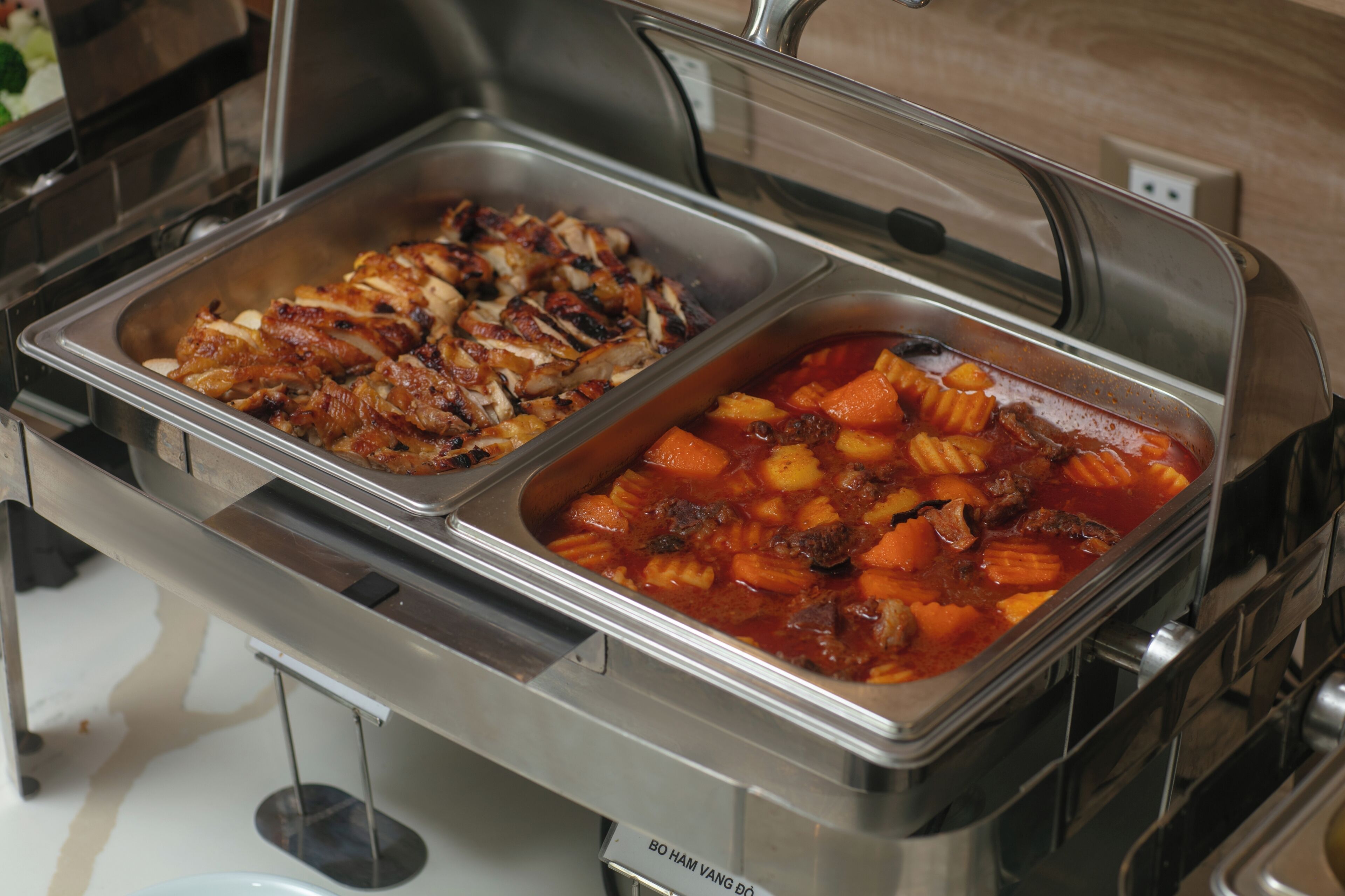 Un buffet comprenant deux plateaux de service en acier inoxydable, l’un contenant de la viande tranchée et l’autre un ragoût de légumes et de viande.