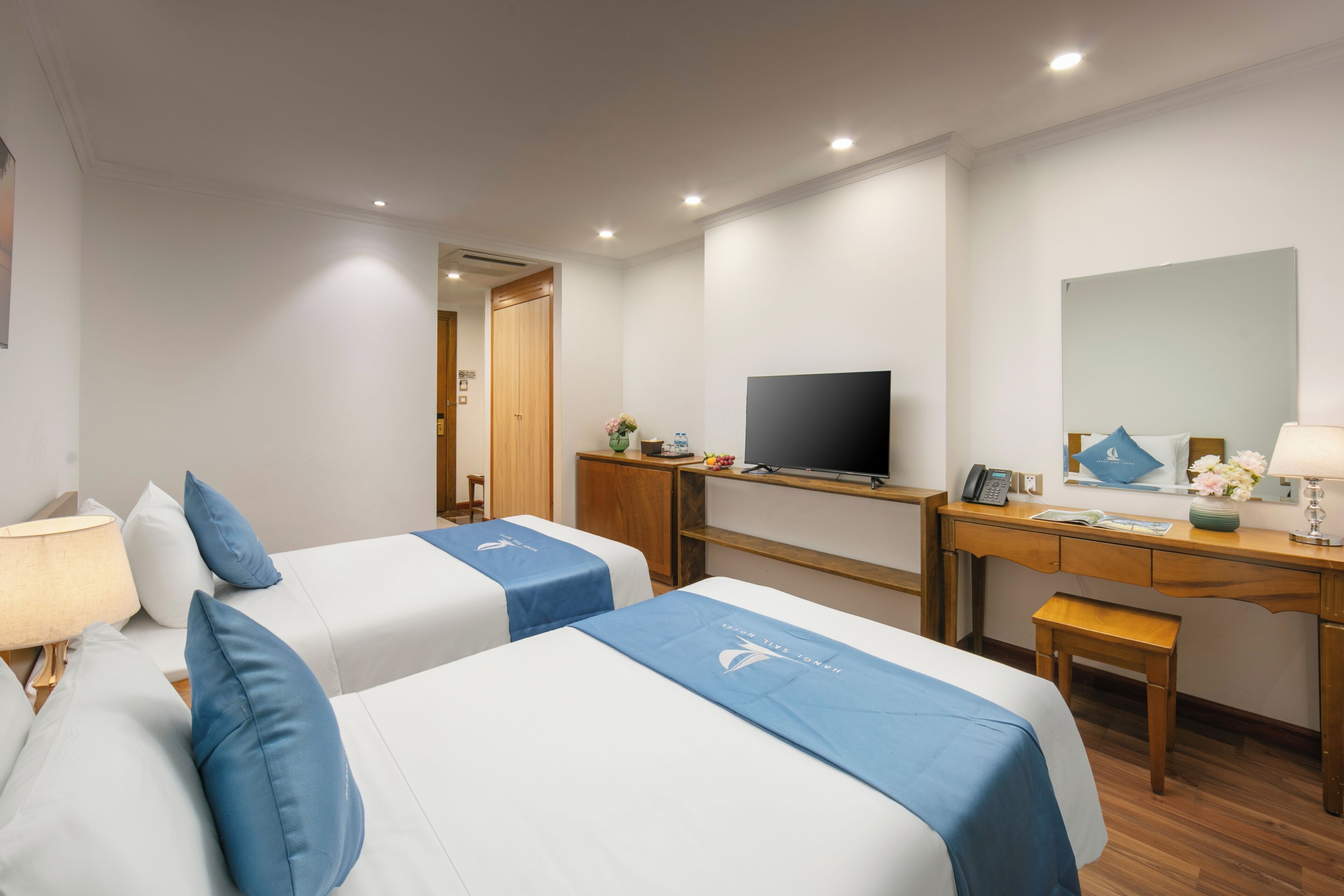 A hotel room with two beds, a desk, a television, a mirror, and a small table.