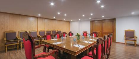Une salle de conférence avec une longue table en bois, des chaises rembourrées de couleur rouge et des spots encastrés au plafond.