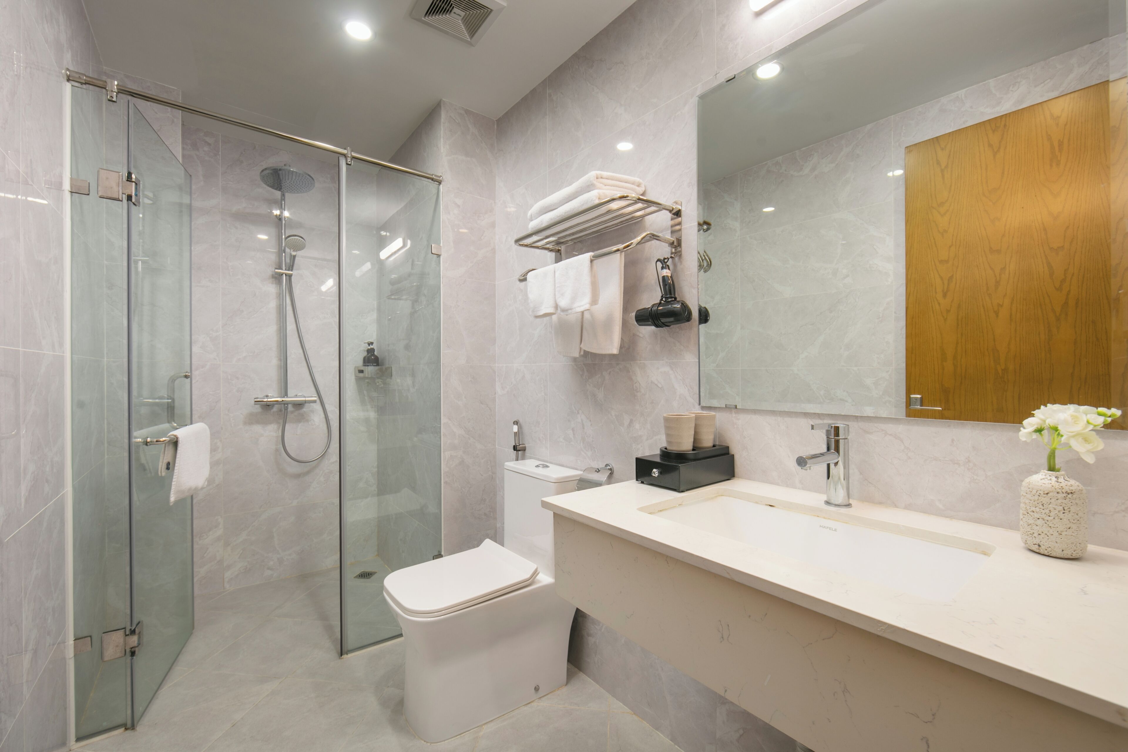Een moderne badkamer met een glazen douchecabine, een wit toilet, een wastafel met spiegel en een houten kast.