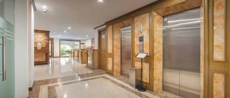Un vestíbulo de hotel con piso de mármol, paneles de madera y dos ascensores.