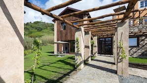 Una estructura rústica de madera con un muro de piedra y un camino empedrado que lleva a una casa con un gran ventanal y una puerta.