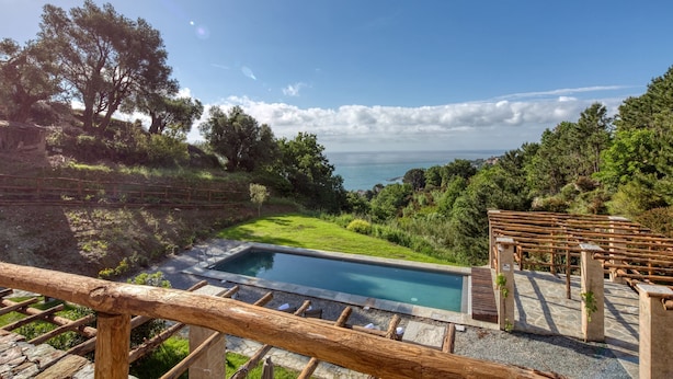 Una piscina con vistas al mar, rodeada de vegetación y una terraza de madera.