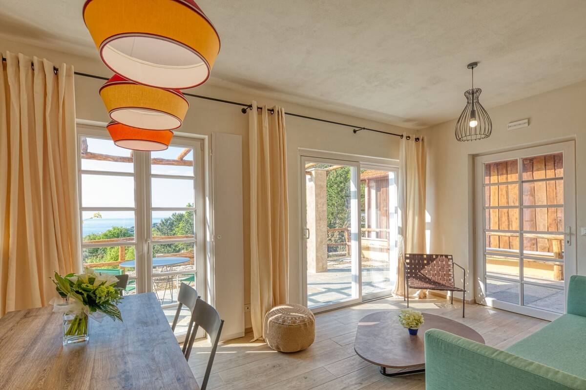 Une pièce spacieuse avec une table en bois, des chaises, un canapé vert et une grande fenêtre donnant sur l’extérieur.