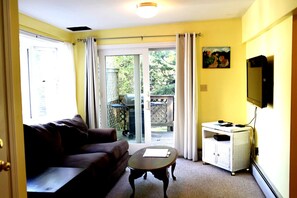 A living room with a sofa, a coffee table, and a TV stand. - 2-story stay w/ king bed and private deck (Portland)