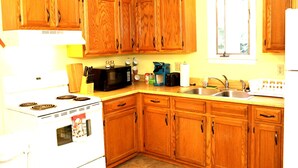 A kitchen with wooden cabinets, a stove, a microwave, a coffee maker, and a sink. - Large 1 bed w/ private deck (Portland)