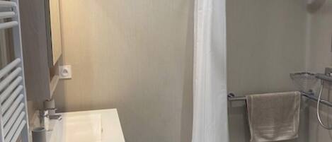 A small bathroom with a white sink, a mirror, a shower with a white curtain, and a blue bath mat.
