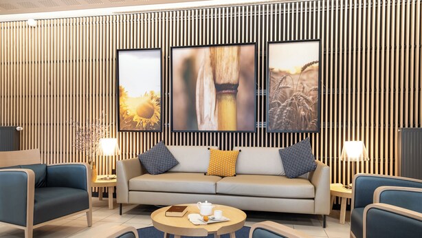 A modern living room with a sofa, two armchairs, a coffee table, and a TV mounted on a wooden wall with vertical slats. - Zenao Appart'hôtels Toulouse Balma (Balma)