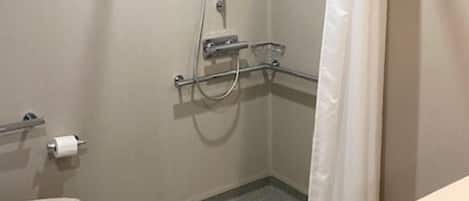 Un espacio de ducha pequeño y cerrado con ducha blanca, ducha de mano y cortina de ducha. Hay un inodoro con una toalla y un lavamanos pequeño con espejo.