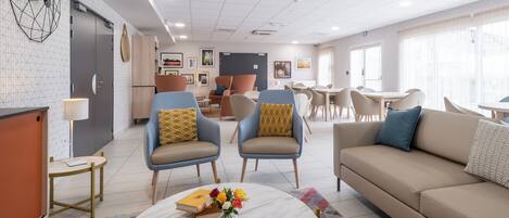 Eine moderne Hotelhalle mit Sitzgelegenheit, einem Esstisch und einer Küche im Hintergrund.