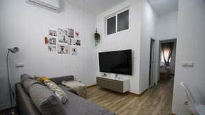 A modern living room with a grey sofa, a flat-screen TV on a white stand, and a small table. - Modern Oasis in Vallecas Seasonal (Madrid)