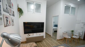 A modern living room with a flat-screen TV, a sofa, a coffee table, and a dining area with a glass table and chairs. - Modern Oasis in Vallecas Seasonal (Madrid)