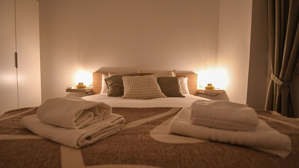 A neatly made bed with pillows, a bedside table with a lamp, and a folded towel on the bed. - Modern Oasis in Vallecas Seasonal (Madrid)