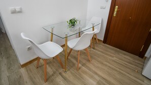 A small dining area with a glass table, white chairs, a potted plant, and a wooden door. - Modern Oasis in Vallecas Seasonal (Madrid)