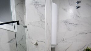A bathroom with marble walls, a glass shower enclosure, a toilet, and a wooden shelf with a plant. - Modern Oasis in Vallecas Seasonal (Madrid)