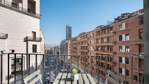 Een hoog gebouw met meerdere balkons, een uitzicht op de straat daaronder, en een heldere lucht.