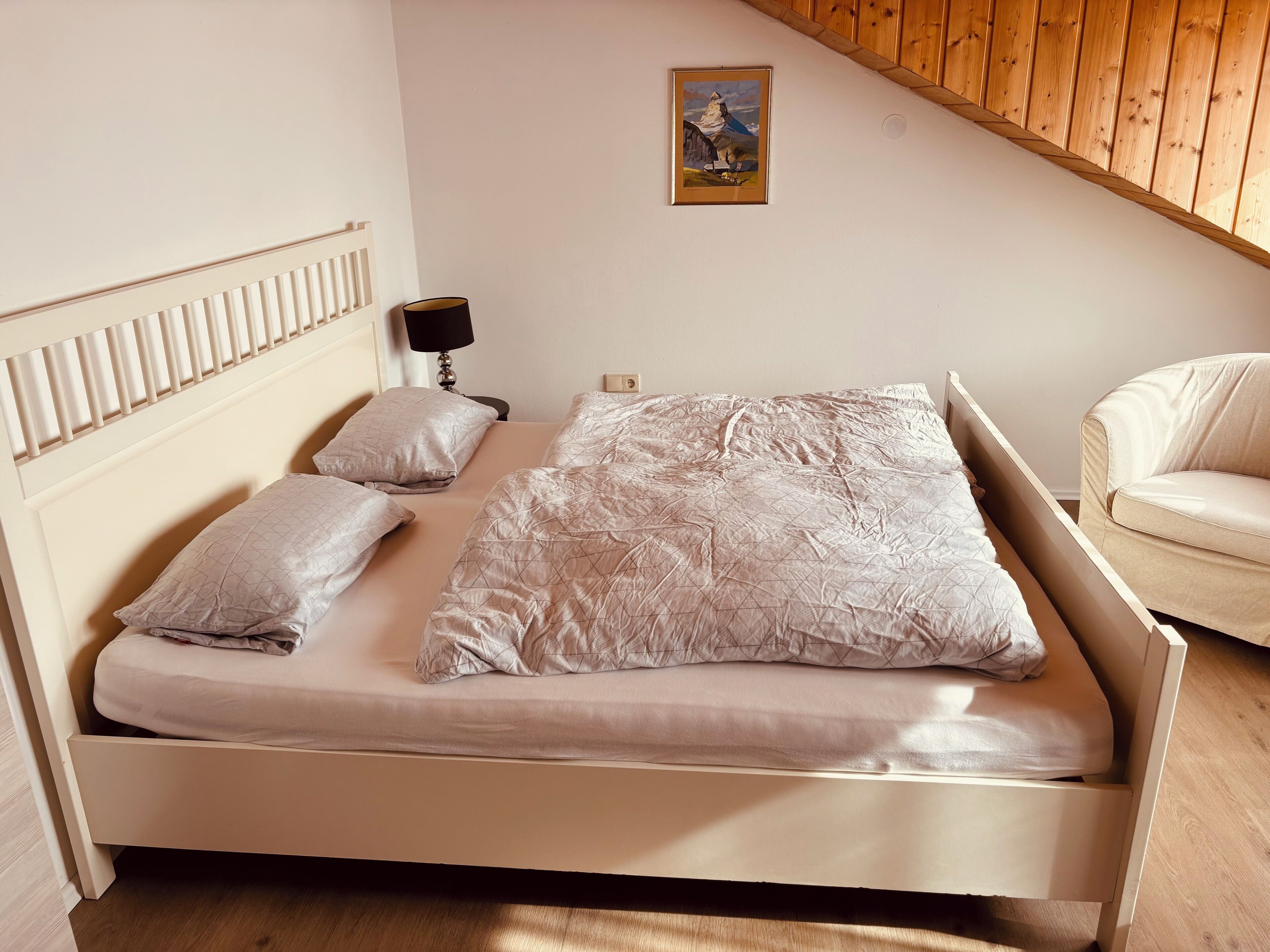 Una cama individual con cabecera, dos almohadas, una lámpara de noche y un cuadro en la pared.