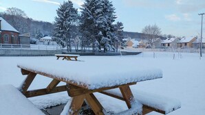 Ein mit Schnee bedecktes Picknicktisch in einem Park, im Hintergrund kahle Bäume und Wohnhäuser.