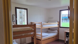 Ein Zimmer mit Etagenbetten, einem kleinen Tisch und einem Fenster mit Blick auf ein Gebäude.