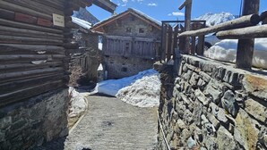 A narrow stone pathway leading to a rustic building with a wooden facade, surrounded by snow and mountains.