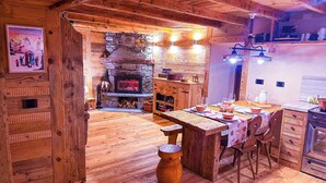 A rustic wooden interior with a stone fireplace, wooden dining table, and a kitchen area.
