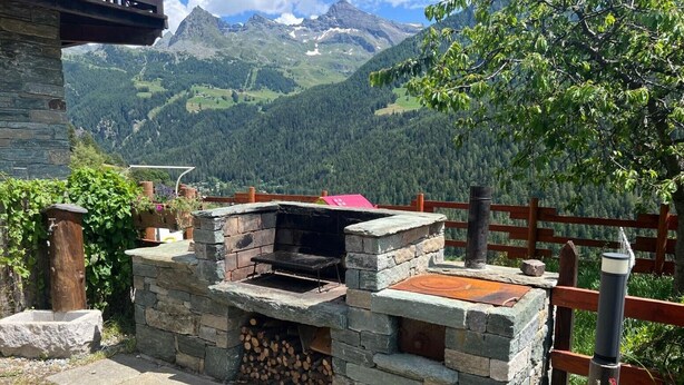 An outdoor stone barbecue grill with a view of mountains in the background.