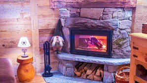 A cozy fireplace with a stone surround, a wooden bench, a lamp, and a shelf with books.