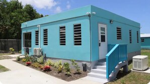 A single-story building with a light blue exterior, a white door, and a blue staircase leading to the entrance. - Modern Home in the Countryside (Pares)