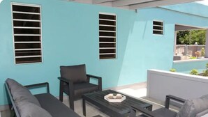 A room with a blue exterior wall, two windows with horizontal blinds, a sofa, a chair, and a small table with a plant. - Modern Home in the Countryside (Pares)