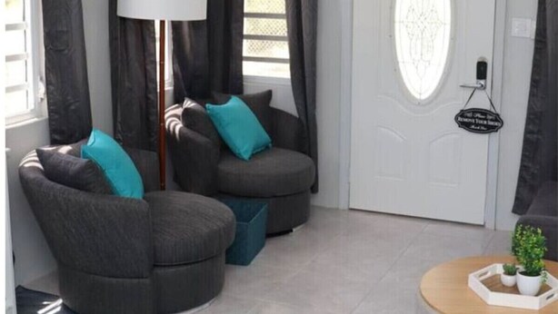 A room with two grey armchairs, a white floor lamp, a round wooden table with a plant, and a door with a sign. - Modern Home in the Countryside (Pares)