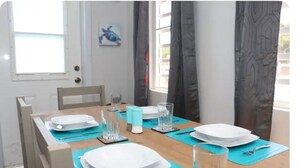 A dining table set with plates, glasses, and cutlery, with a window and curtains in the background. - Modern Home in the Countryside (Pares)