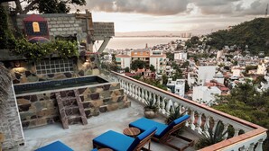 Terraza en la azotea con muros de piedra, una piscina y sillones de descanso azules.