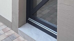 A modern door with a glass panel and a handle, set in a building with a plain exterior wall and a window to the left.