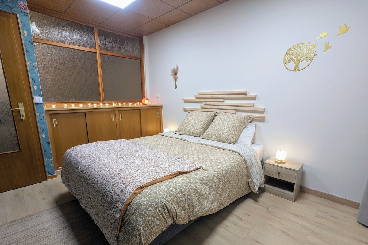 A bedroom with a bed, bedside table, and a window with curtains.