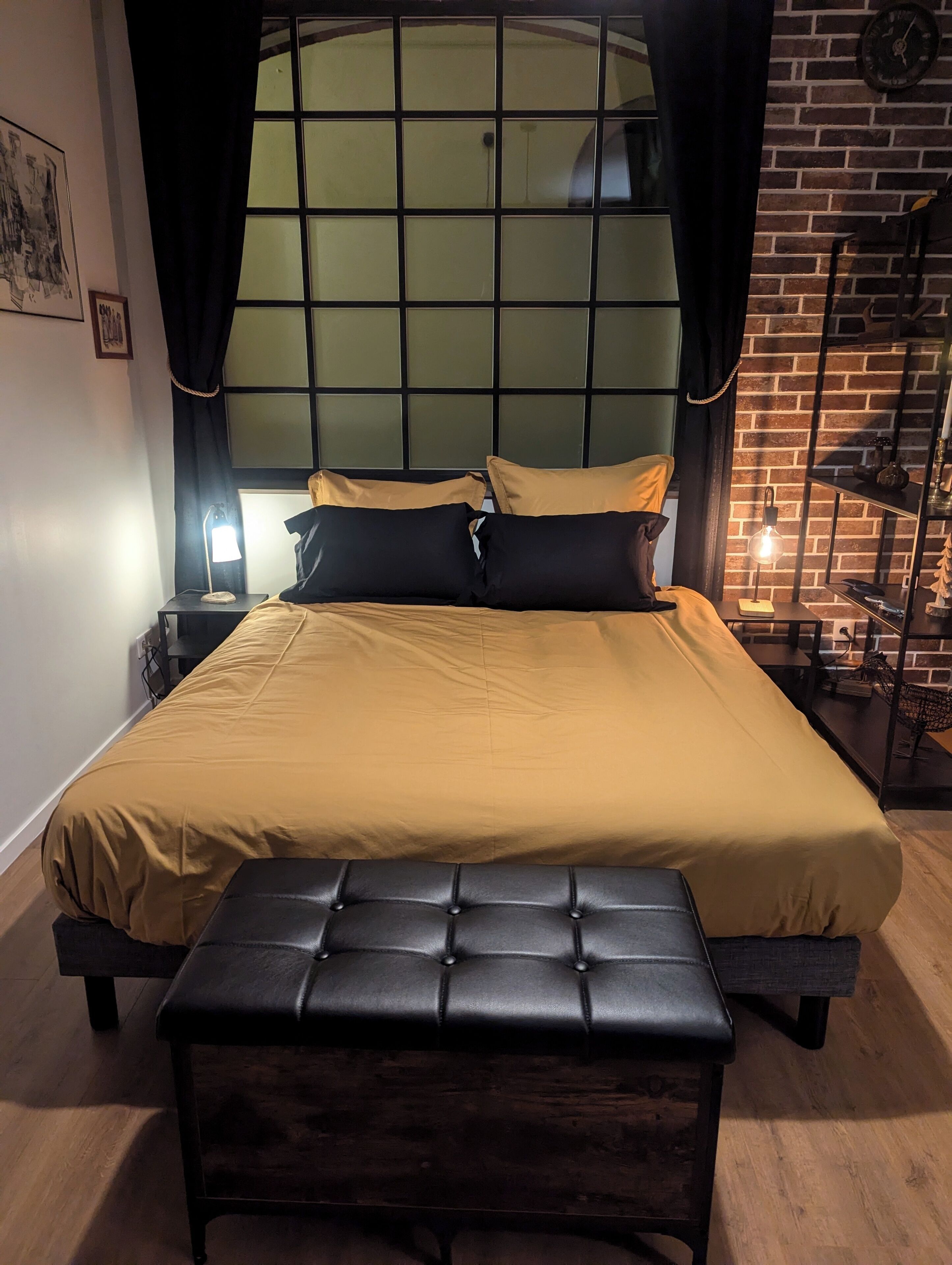 Una cama con cabecera, un banco y una mesita de noche con lámpara.