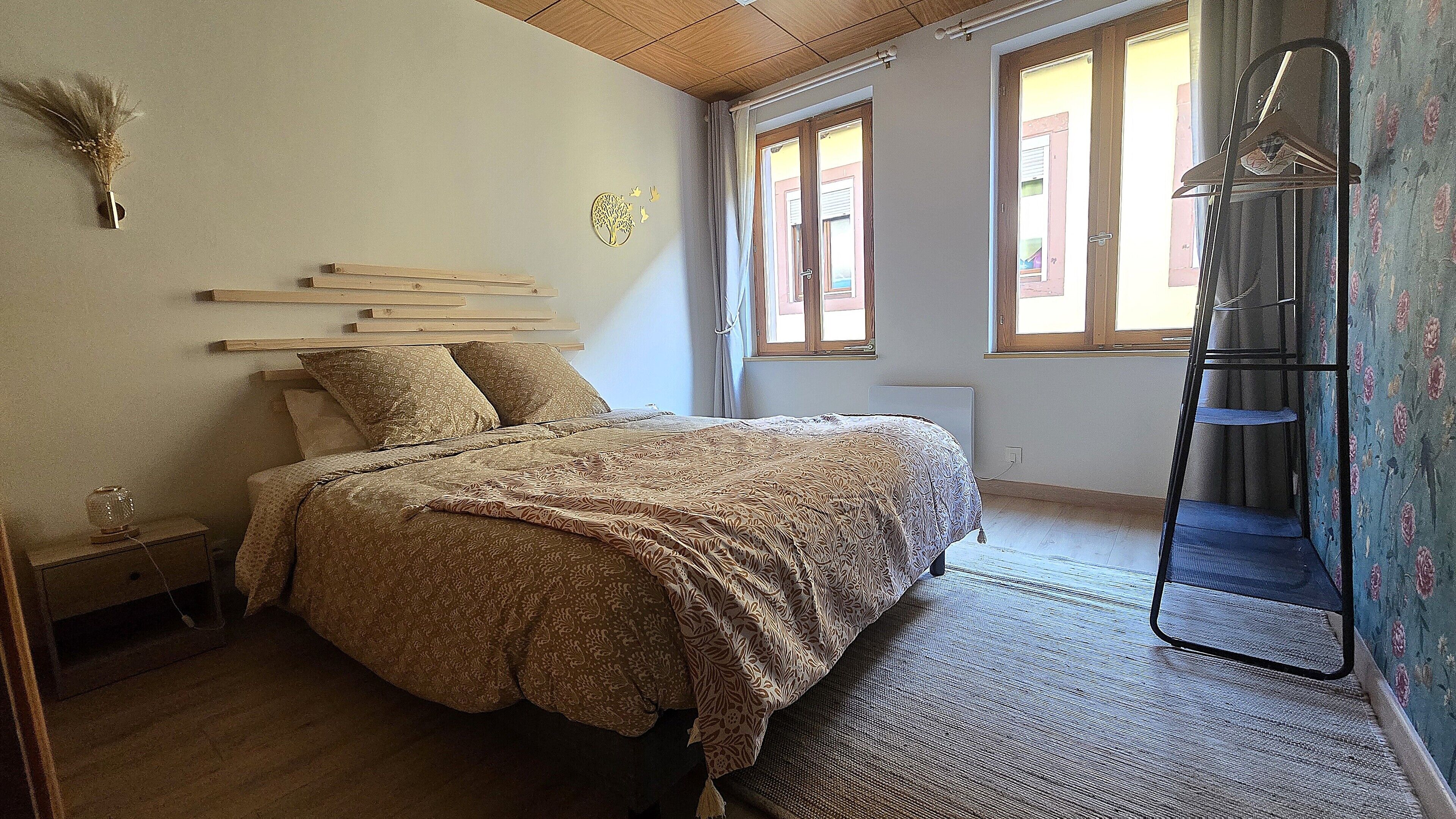 A bedroom with a bed, a bedside table, a lamp, a radiator, a window, and a wardrobe.