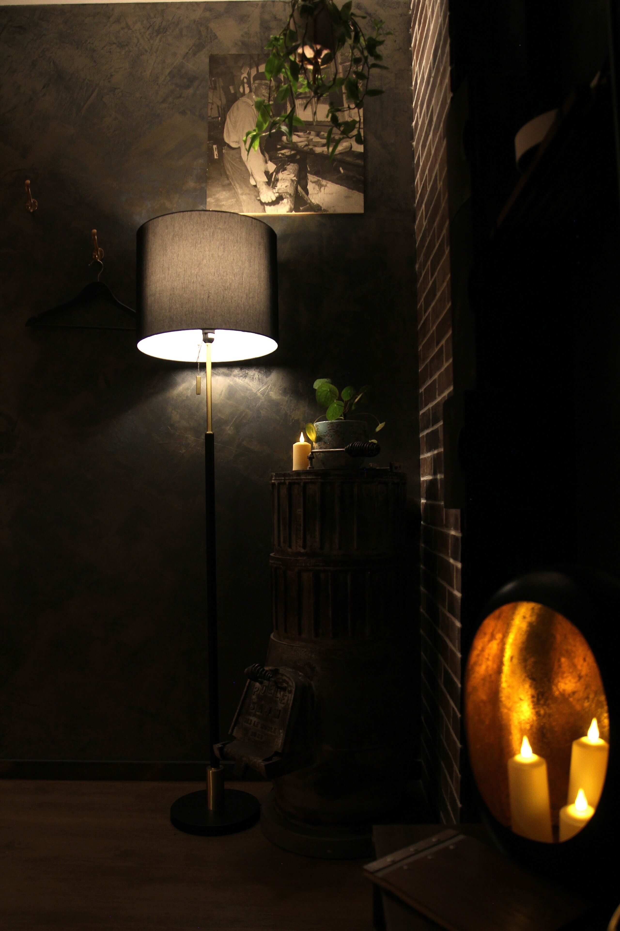 A dimly lit room with a floor lamp, a small table with candles, and a framed picture on the wall.