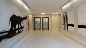 Un couloir avec deux ascenseurs, des murs blancs et des œuvres d’art abstraites accrochées aux murs.